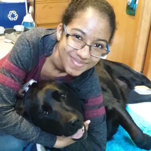 Kayla hugs a black labrador while smiling